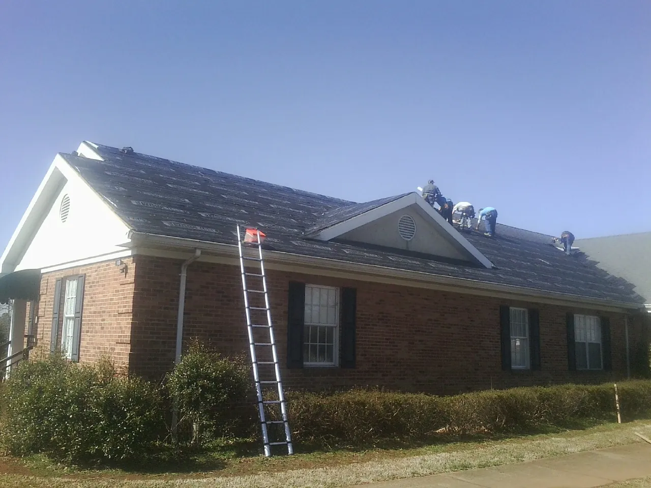Crew tearing shingles off a brick ranch roof with a ladder set — Emergency Roof Repair work by our crew in Braintree