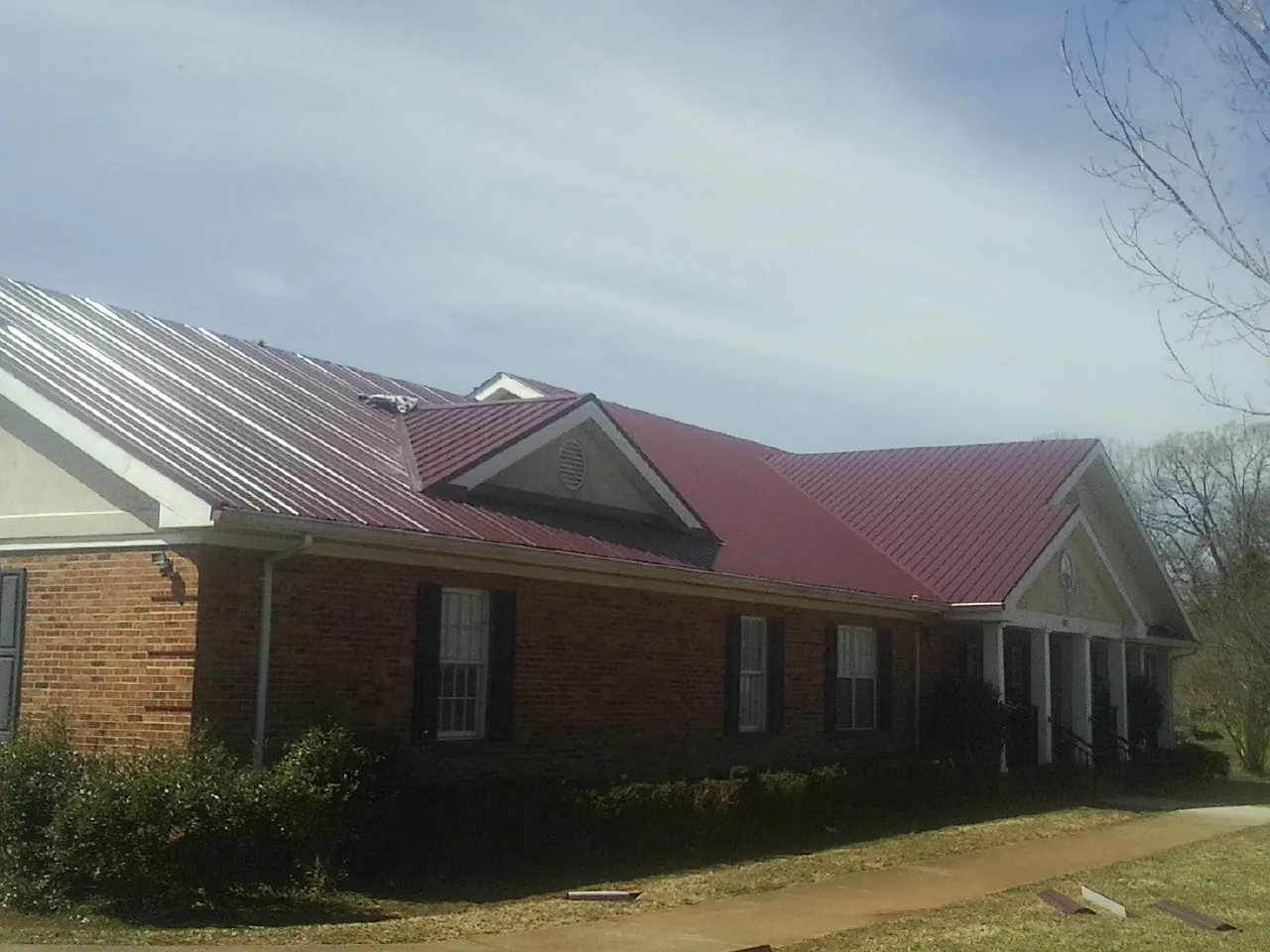 Red metal roof with gabled entries on a long brick building, from a Hail Damage Roof Repair job in Braintree