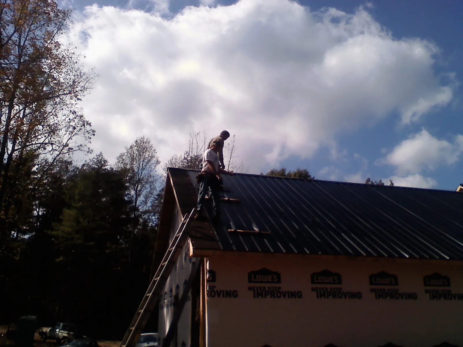 Roofer fastening dark metal panels high against a cloudy sky, from a Roof Inspection job in Braintree