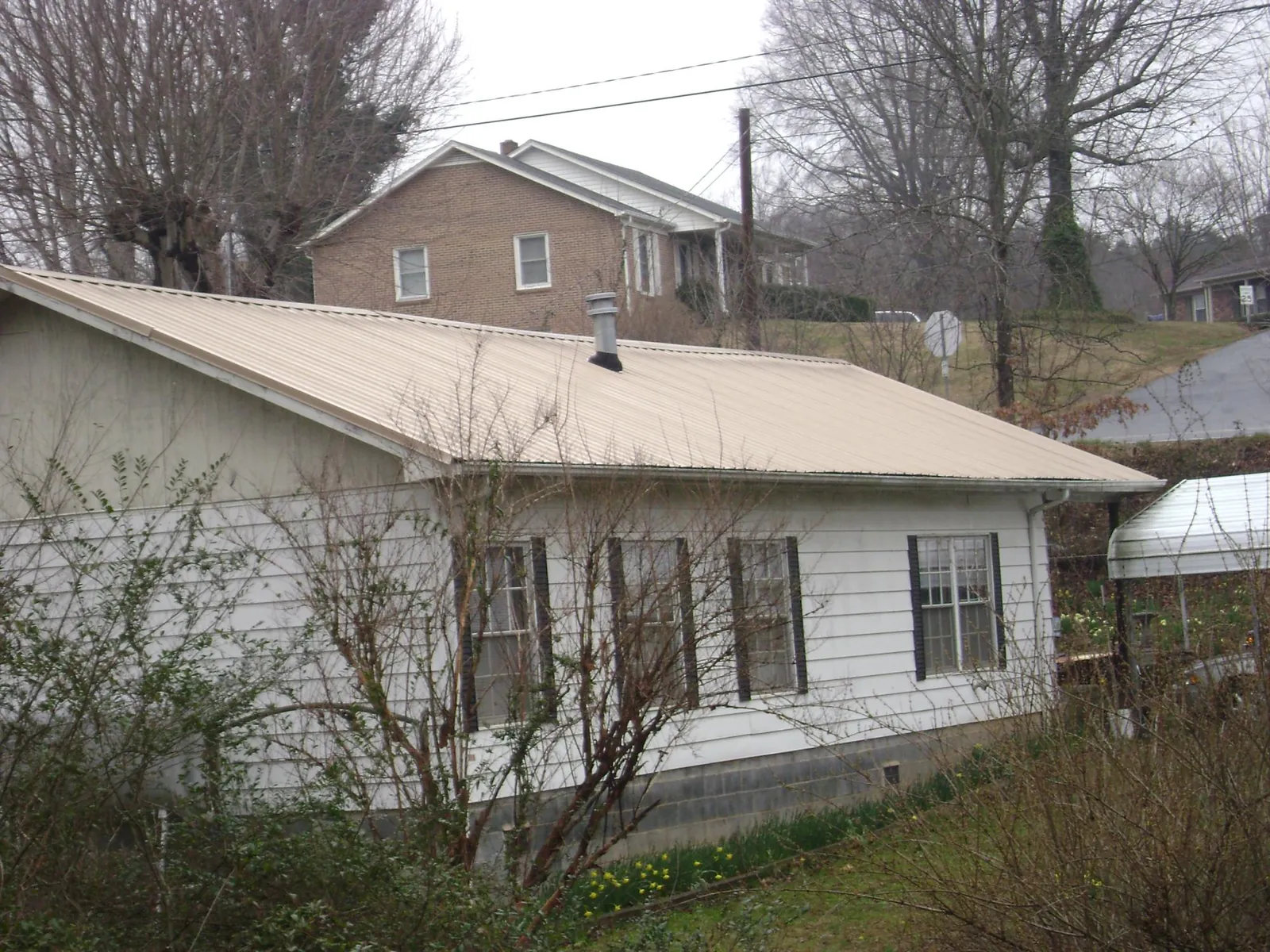 Tan metal roof on a white sided house set into a hillside — Commercial Roofing by Roofing Brothers in Braintree